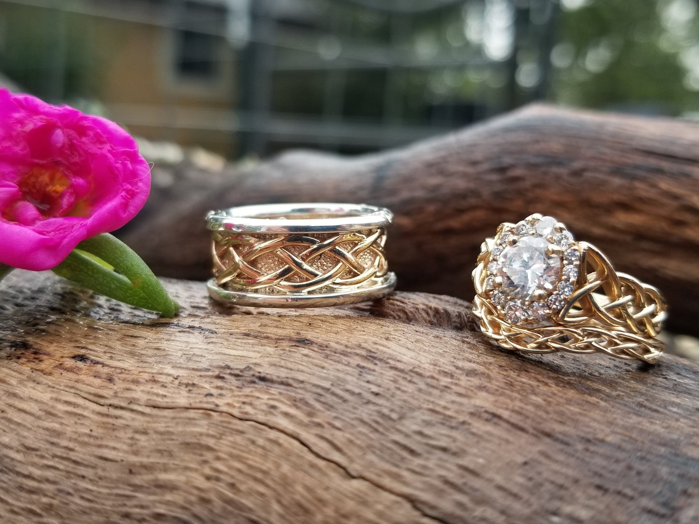 A braided two-tone wedding band beside a matching braided engagement ring on driftwood