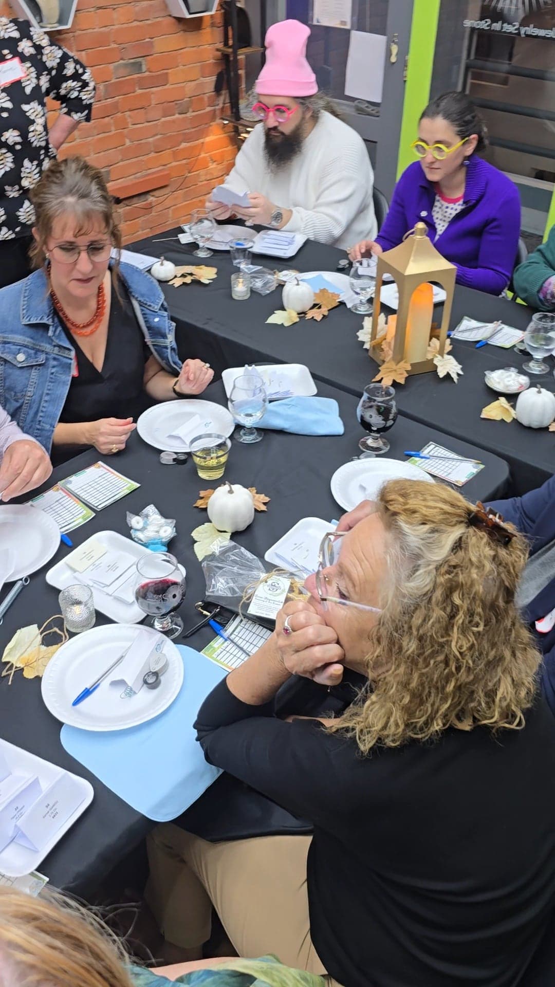 Guests around tables set with candle lanterns, white pumpkins and autumn leaves, studying gemstones and score cards