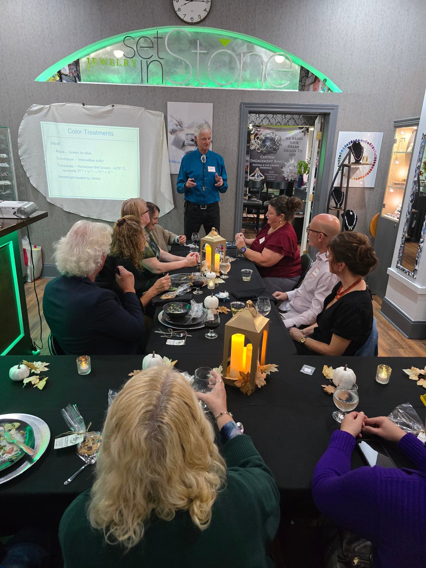 Scott Sucher speaks to guests around a long candlelit table beneath the Jewelry Set in Stone sign