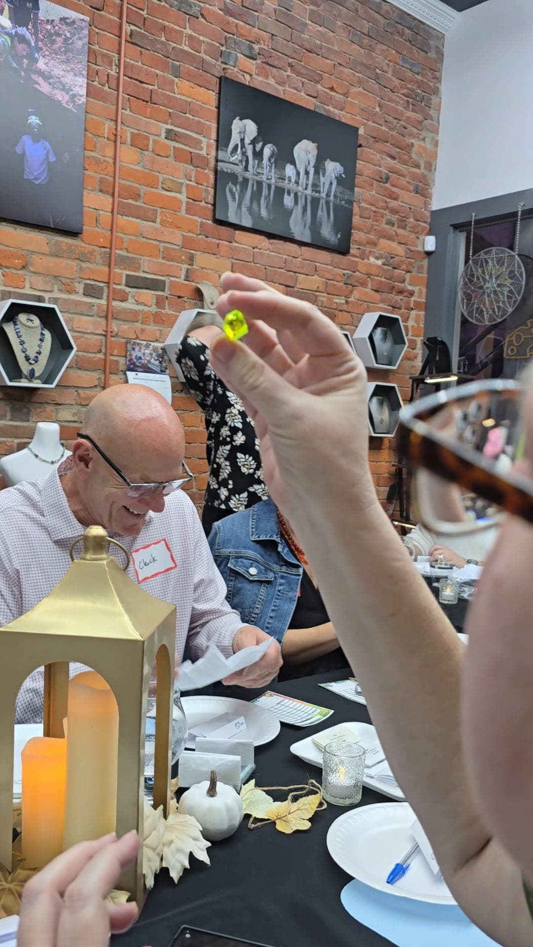 A guest holds a bright yellow-green gemstone up to the light while another guest smiles at the table