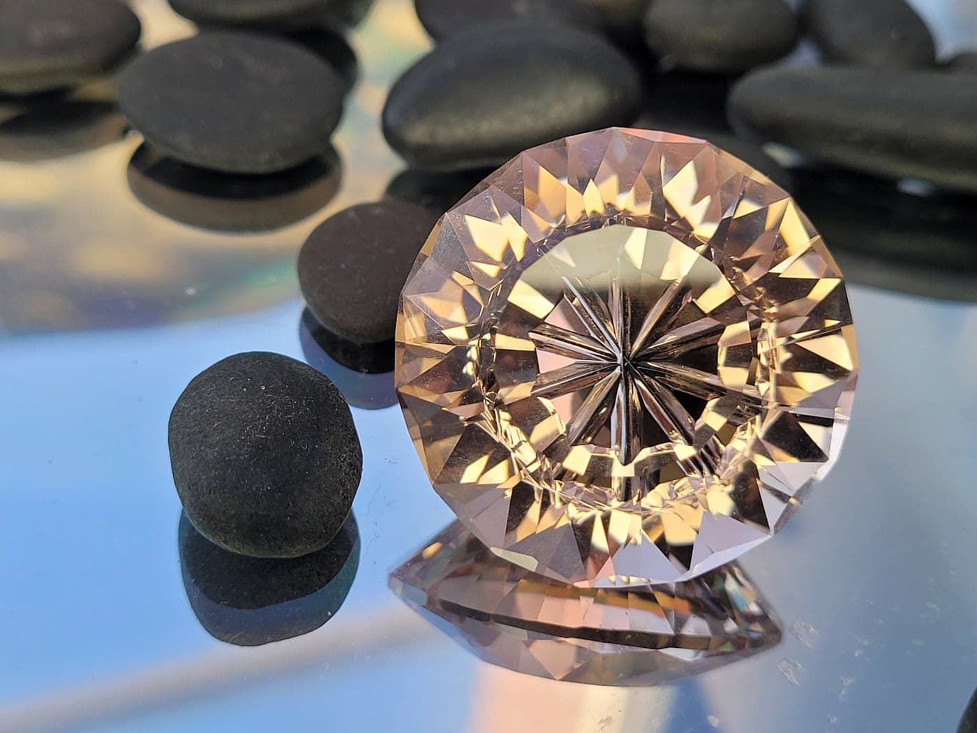 A large round peach-colored gemstone with a star carved into its center, beside a smooth black stone