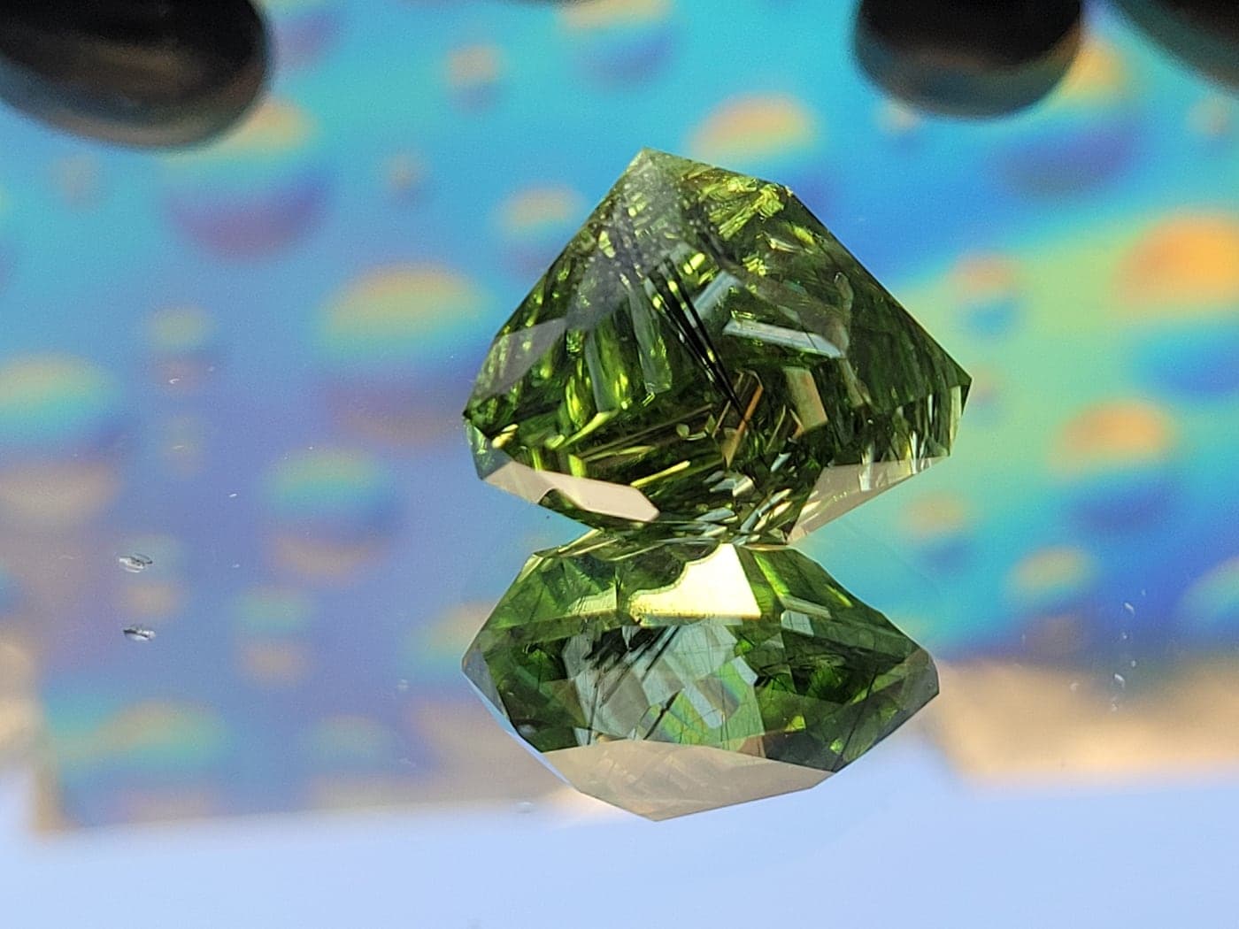 A vivid green gemstone with fine needle-like inclusions, faceted in an unusual shape