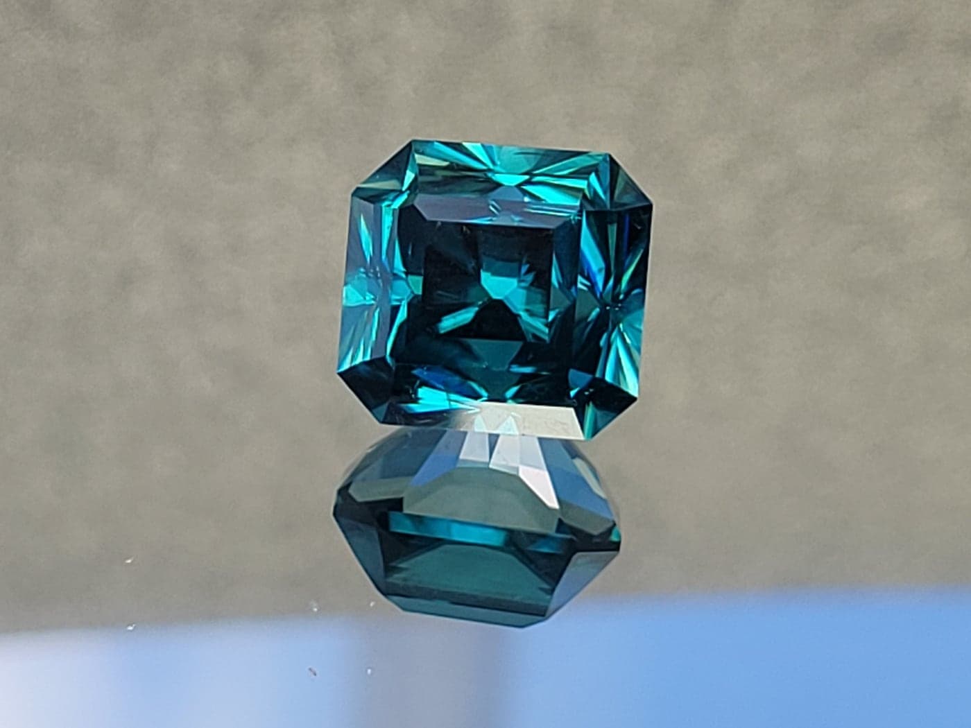 A square teal gemstone flashing blue and green