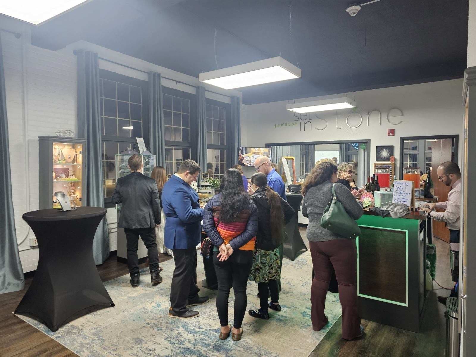 Guests mingling in the studio during an evening event, browsing jewelry cases and chatting at the glowing green bar