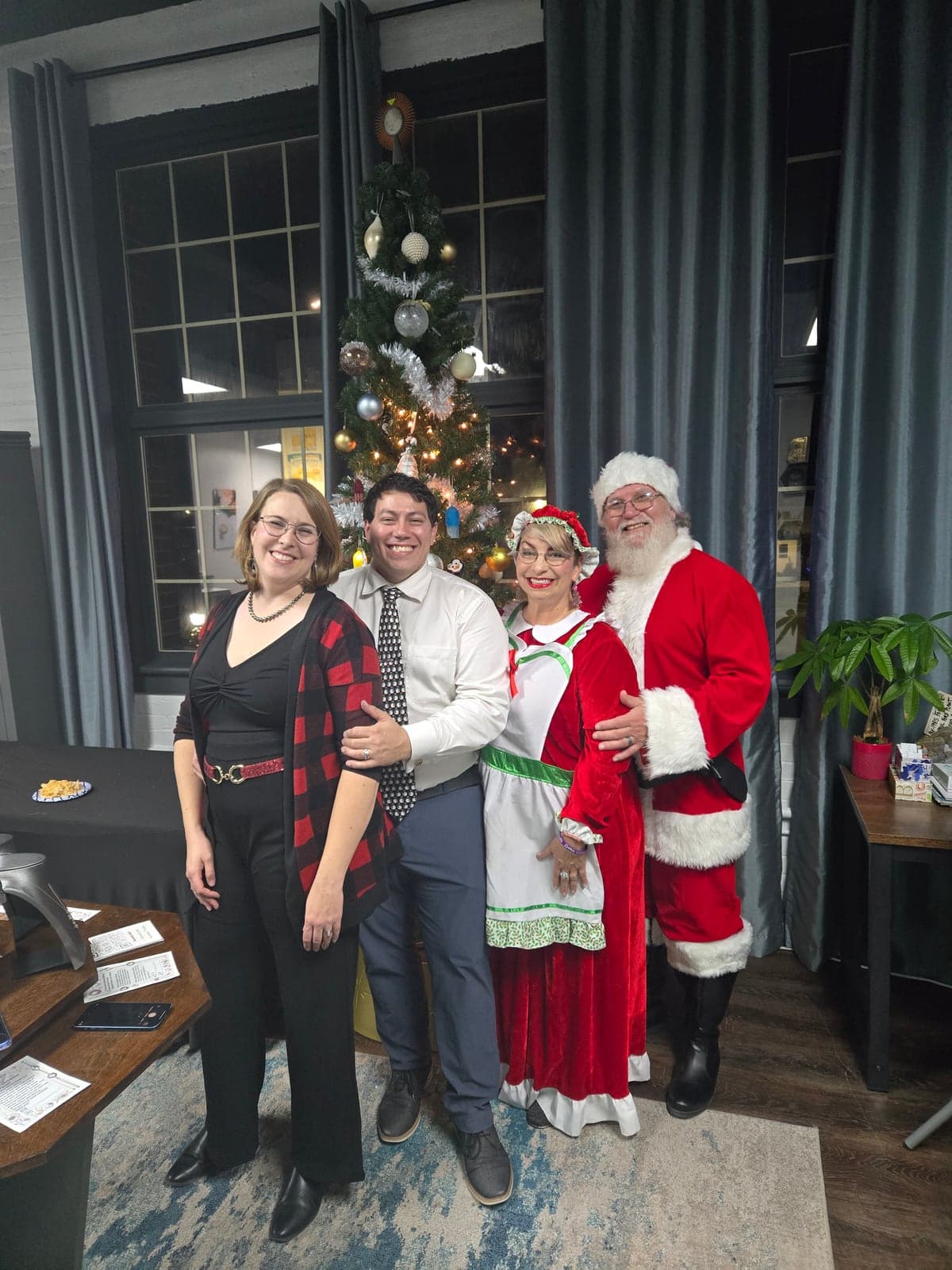Santa and Mrs. Claus smiling with two guests in front of a lit Christmas tree at a past studio Christmas party