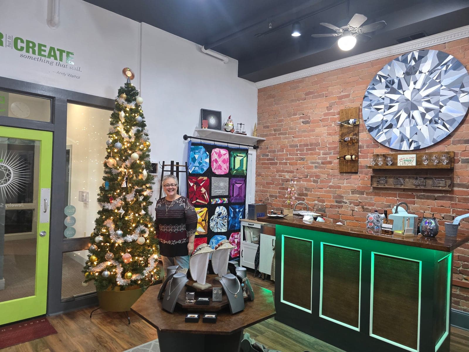 The studio decorated for Christmas: a tall tree with gold and silver ornaments beside a quilt of colorful gemstones and a painted diamond on the brick wall